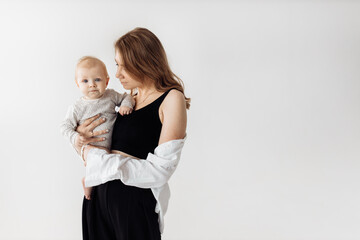 Young beautiful woman holding a cute baby girl in arms, smiling. Lovely toddler looking at the camera with big interest, mother spend time with little daughter, posing in studio