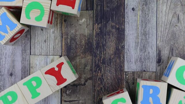 Colourful alphabet letters on wooden cubes with word - Happy - in a diagonal line with additional blocks decorating the corners of the frame. Stop motion, top view