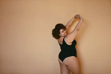 Beautiful curvy oversize African black woman afro hair posing in black bodysuit on beige brown background isolated, body imperfection, body acceptance, body positive and diversity concept. Copyspace.