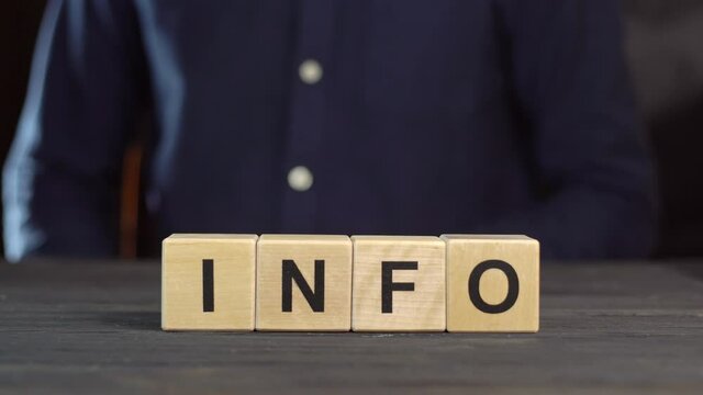 A man in a shirt composes the word INFO from wooden cubes, close up