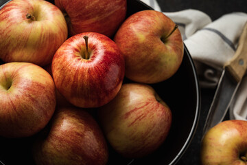 Apples in a bowl on a black table with a knife.