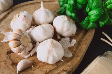 
Garlic bulbs on a wooden board on a black background, with dried garlic and a bunch of basil. Diet. Condiments and spices for Mediterranean cuisine.
