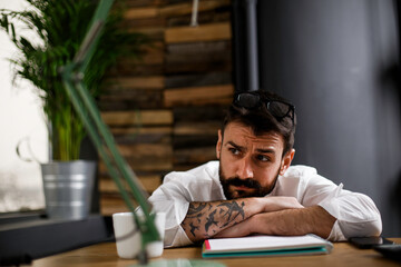 Obraz premium Exhausted businessman working with laptop at office. Tired man sitting at office desk working on laptop computer