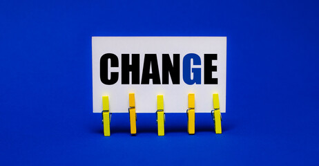On a bright blue background on yellow clothespins, a white card with the text CHANGE