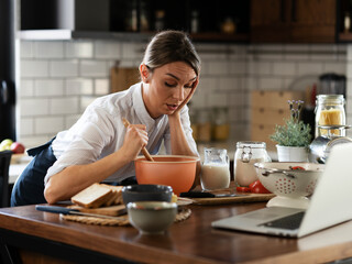 Young woman cooking in the kitchen. Beautiful woman watching movie on laptop while cooking