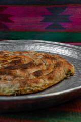 homemade Bosnian pie burek with meat in a traditionally made vessel and old homemade Persian style rug and wooden plate
