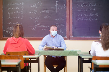 Students in protective face masks studying in classroom with teacher. Precautions in coronavirus pandemic