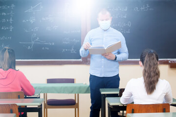 Students in protective face masks studying in classroom with teacher. Precautions in coronavirus pandemic