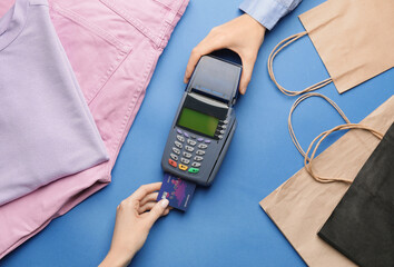 Female hands with credit card, payment terminal and clothes on color background