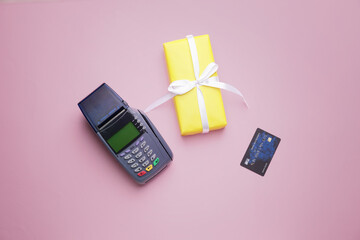 Payment terminal with credit card and gift box on color background