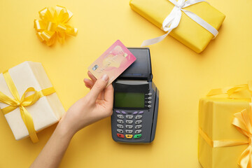 Female hand with credit card, payment terminal and gifts on color background