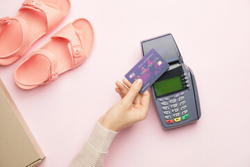 Female hand with credit card, payment terminal and pair of sandals on color background