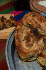 homemade Bosnian pie burek with meat in a traditionally made vessel and old homemade Persian style rug and wooden plate