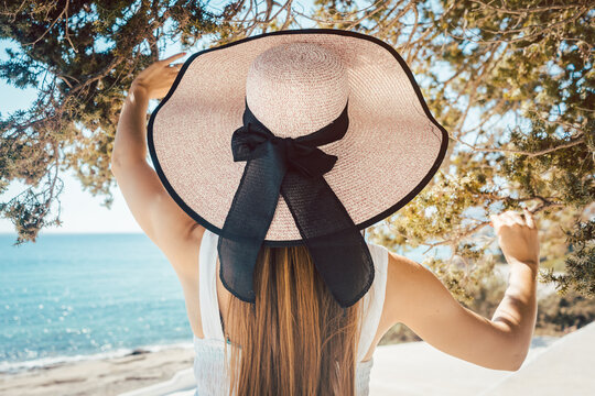 Rear View Of Woman With Hat Standing At Shore Of Beach
