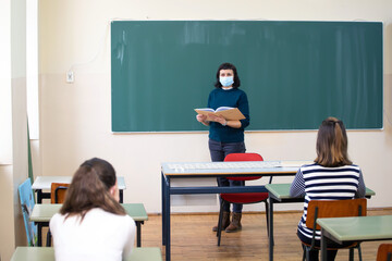 Students in protective face masks studying in classroom with teacher. Precautions in coronavirus pandemic