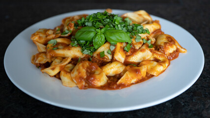 ready to eat, homemade tortelloni stuffed with prosciutto in tomato sauce with basil