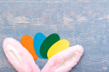 Happy Easter concept. Multicolored paper Easter eggs and pink bunny ears on a wooden blue background