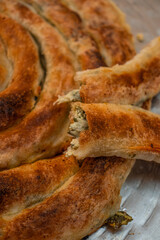 homemade Bosnian pie burek with meat in a traditionally made vessel and old homemade Persian style rug and wooden plate