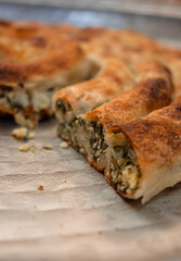 homemade Bosnian pie burek with meat in a traditionally made vessel and old homemade Persian style rug and wooden plate