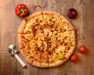 Pizza on a wooden table with red peppers, tomatoes, onion a a roller knife