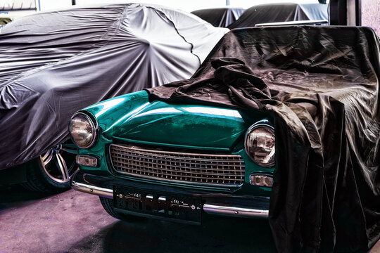 Italienischer gr&uuml;ner Oldtimer-Sportwagen. Bis zur Motorhaube mit Tuch bedeckt. Steht neben anderen abgedeckten Oldtimern in Garage