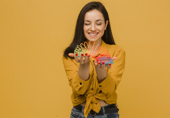 Photo of cute female with nice smile holds slinky. Wears yellow shirt, isolated yellow color background