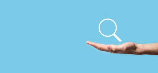 Male hand holding magnifying glass ,search icon on blue background. Concept search engine...