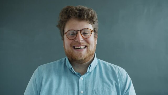 Portrait of joyful young man laughing looking at camera then making funny faces on gray background. Good mood and positivity expressions concept.
