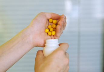 A young girl's hands hold round yellow vitamins in the palm of her hand. A woman's hand holds the medicine and pours the pills into a bottle. Healthy lifestyle, disease prevention. Food supplement.