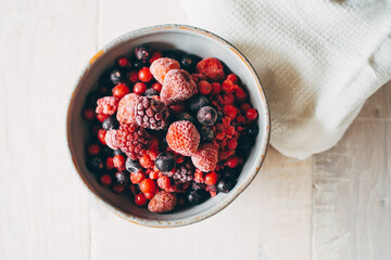 frozen berries in white ceramic bowl on wooden background