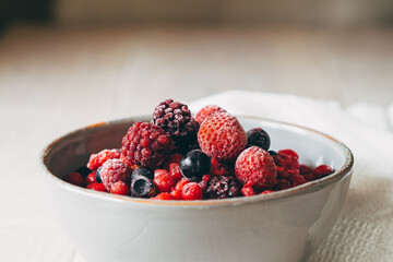 frozen berries in white ceramic bowl on wooden background