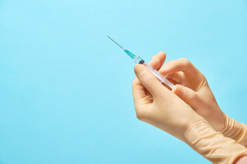 Doctor's hands in gloves hold a syringe with a needle on a blue background. Syringe and vial human hand about to make vaccine.Vaccines against pneumonia covid19.