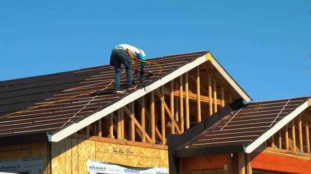 Worker nailing wood slats for installation of ceramic roofing tiles on residential building using an air nail gun- new home roof construction in California shot in 4K