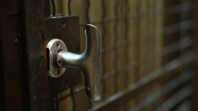 Antique elevator going up and arriving at floor. A hand opens and closes the door knob and the wooden gate. Close up
