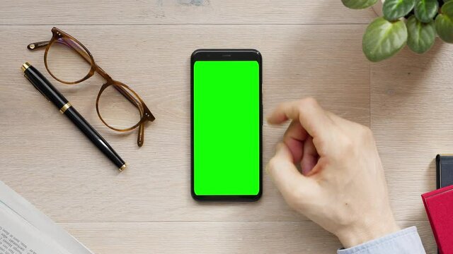 Young Entrepreneur Working from Home using Phone with Green Screen. Smartphone on Light Wooden Home Office Desk. Top View, glasses, Fountain Pen. Scrolling, Tapping Gestures. 4k Flat lay Close-up