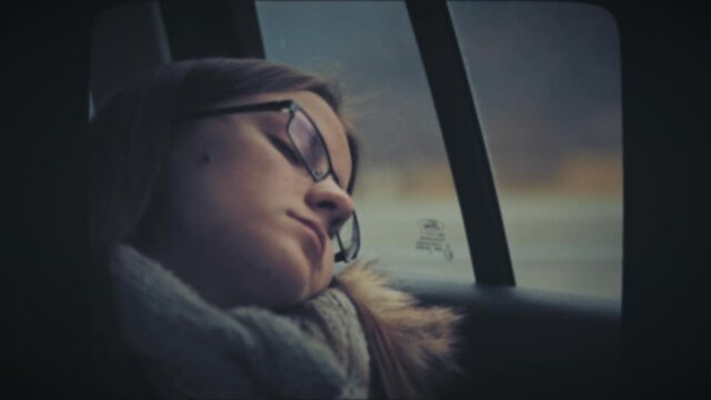 Young woman with sunglasses sleeping in back seat of moving car. Vintage Film Look. 