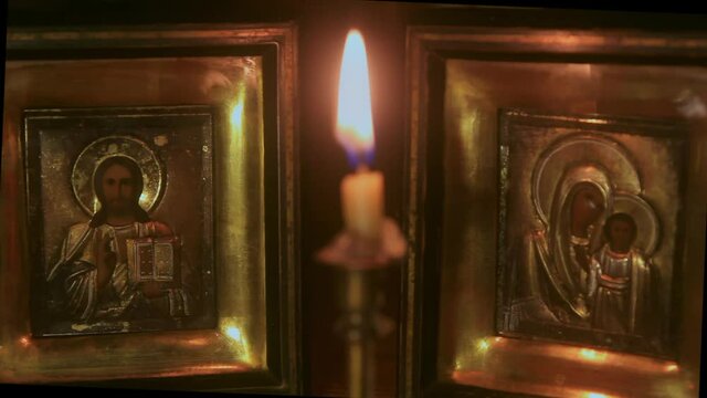 light a candle in a candlestick of another candle in front of the old Christian icons of the Mother of God and Nicholas the Wonderworker