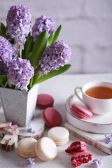 Obraz na płótnie Canvas Spring atmosphere. Flowers in a vase, macaroni, chocolate and a cup of tea on wooden white boards on a light table. Lilac hyacinths. Background image, copy space, vertical, rustic