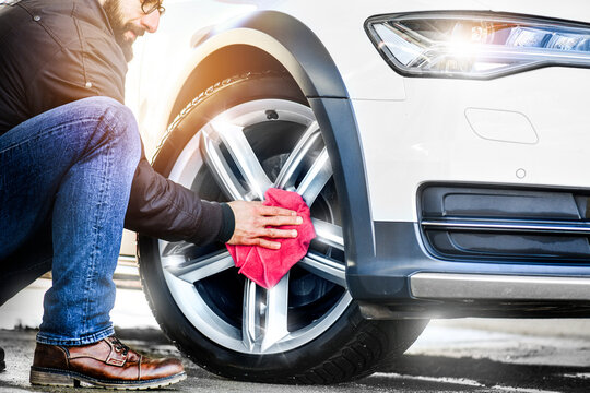 Car detailing close up. Man holds red microfiber in hand and polishes the wheel alloy tire.