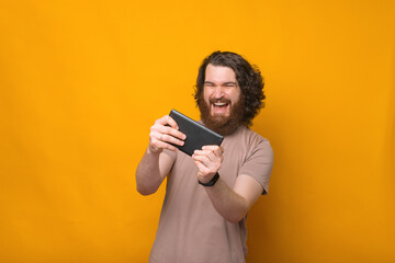 Cheerful young bearded man with curly hair playing games at tablet