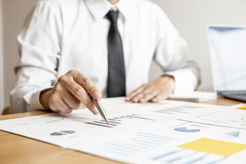 A close-up of a financial businessman holding a pen and pointing at the information sheet on his desk, reading the company's financials to make a financial plan. Financial concept.