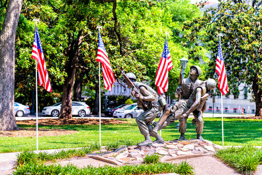 Raleigh, USA - May 12, 2018: North Carolina Vietnam Veteran's Monument memorial with three soldiers carrying rifles, wounded comrade with row of American flags at union square park