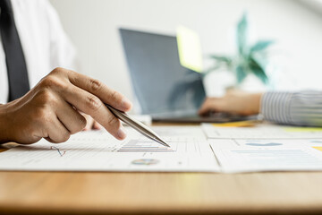 A close-up of a financial businessman holding a pen and pointing at the information sheet on his desk, reading the company's financials to make a financial plan. Financial concept.