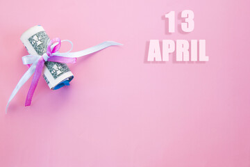 calendar date on pink background with rolled up dollar bills pinned by pink and blue ribbon with copy space. April 13 is the thirteenth day of the month