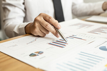 A close-up of a financial businessman holding a pen and pointing at the information sheet on his...