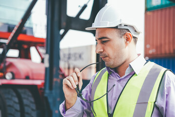 Caucasian engineer foreman holding sunglasses at container warehouse and forklift truck background. men at work on construction site. logistic business or shipping delivery