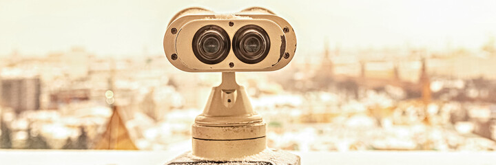 Coin-operated binoculars on the observation deck overlooking the city from a height at sunset. Winter, snowfall.