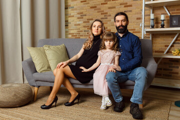 Happy young father, mother and daughter sit on wicker sofa at home.