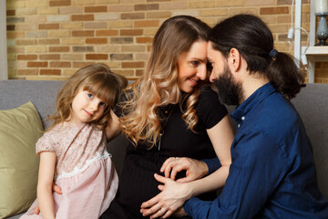 Happy young father, mother and daughter sit on wicker sofa at home.