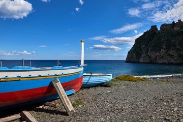 Fototapeta na wymiar Typical colored wooden fishing boat in front of the fortress of Sant'Alessio Siculo in the province of Messina on a sunny day in early spring